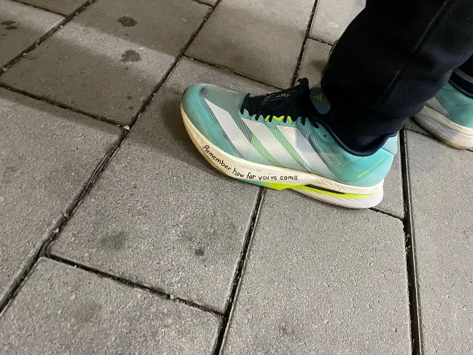 Racing shoe with the words remember how far you have come written on the midsole