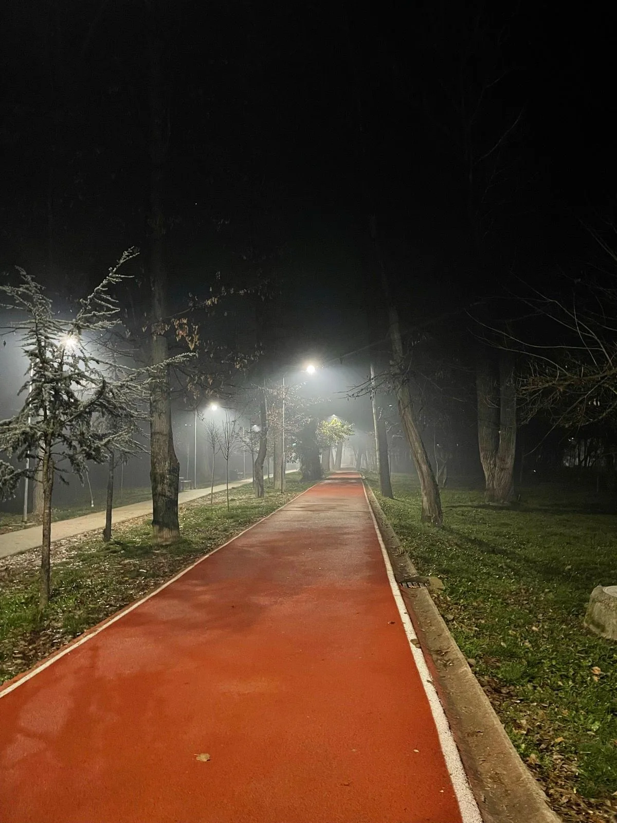 Empty red running track glowing under the lights on a foggy night
